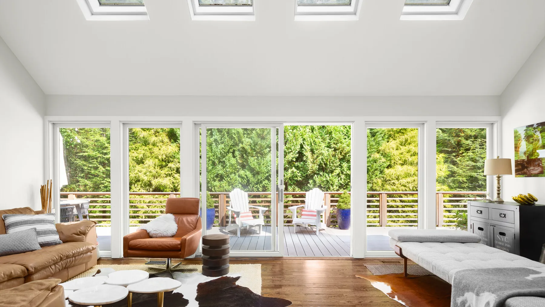 A bright living room opens onto a deck through wide windows, with seating and a daybed.