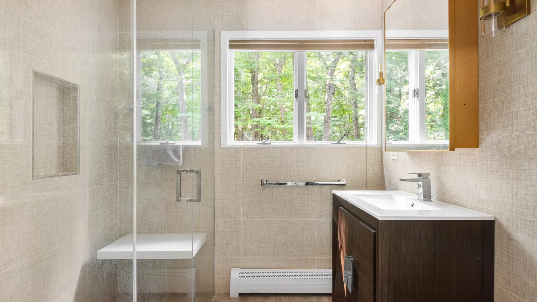 A bright bathroom has a vanity and large windows overlooking greenery.