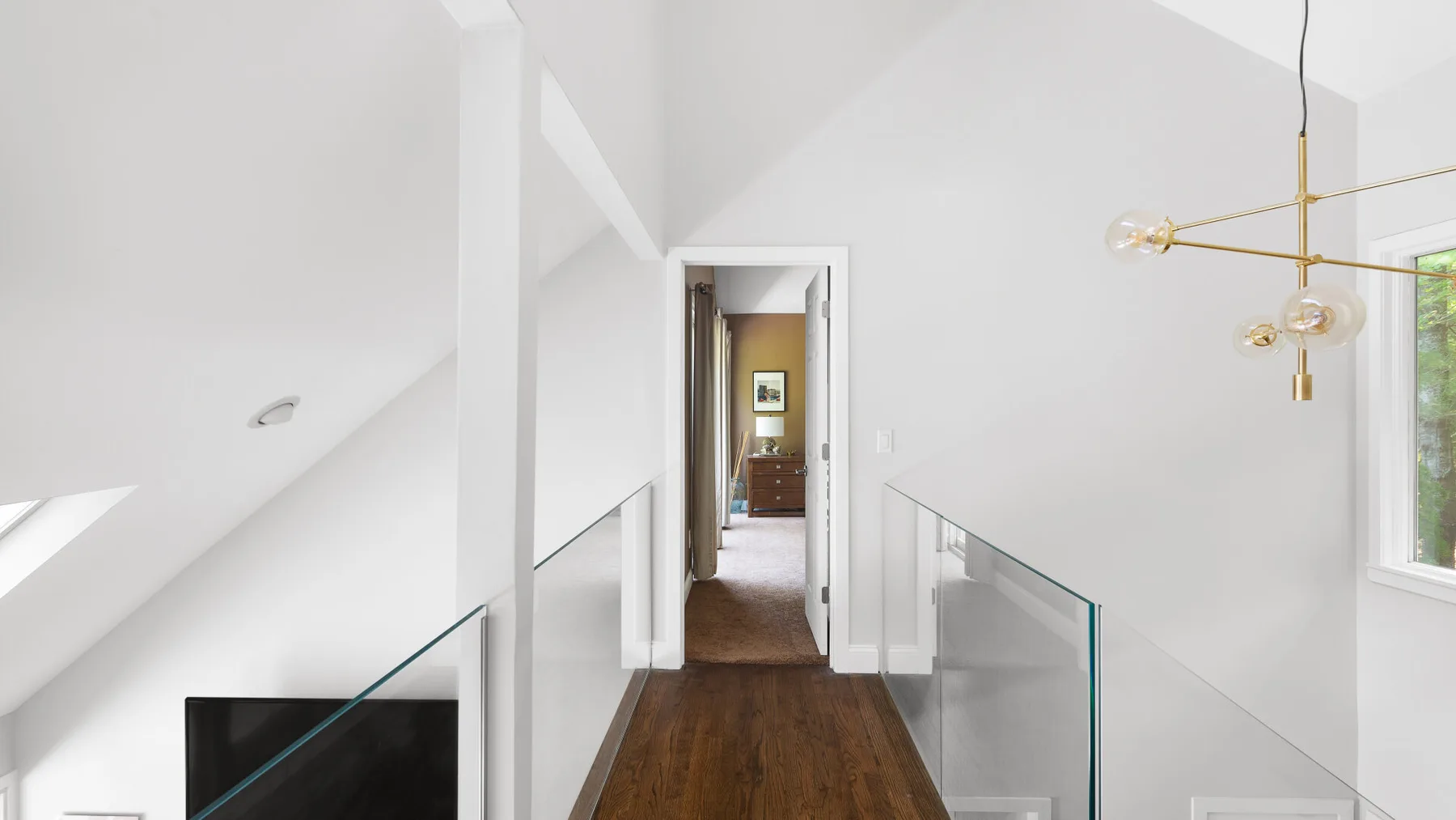 A bright loft hallway with glass railings and a wooden floor.