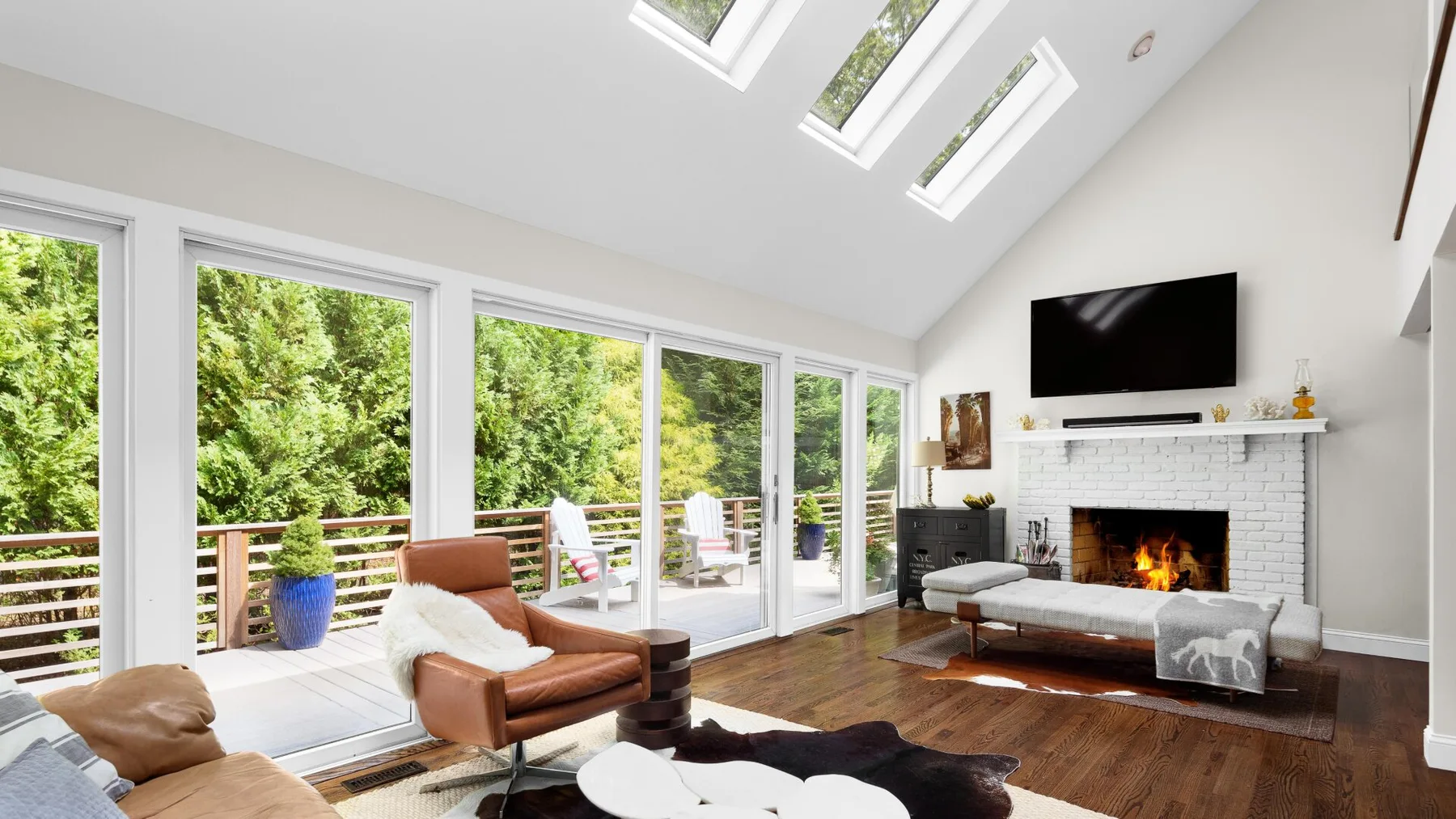 A bright living room with large windows, seating, and a fireplace.