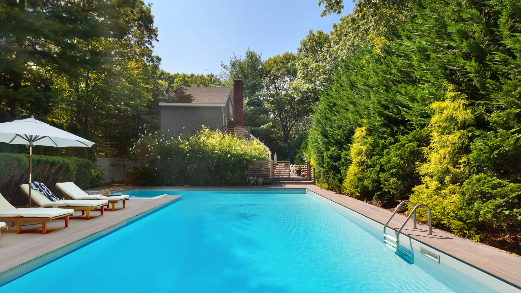 A swimming pool is surrounded by a deck, lounge seating, and trees.