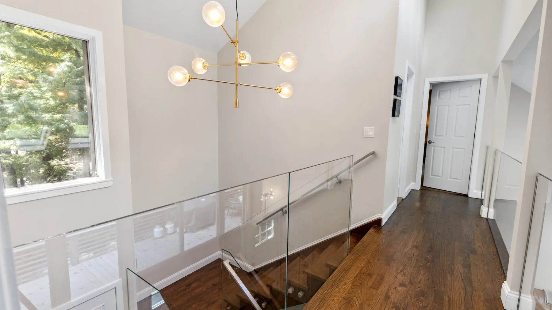 A bright hallway with a glass railing beside a wooden staircase.