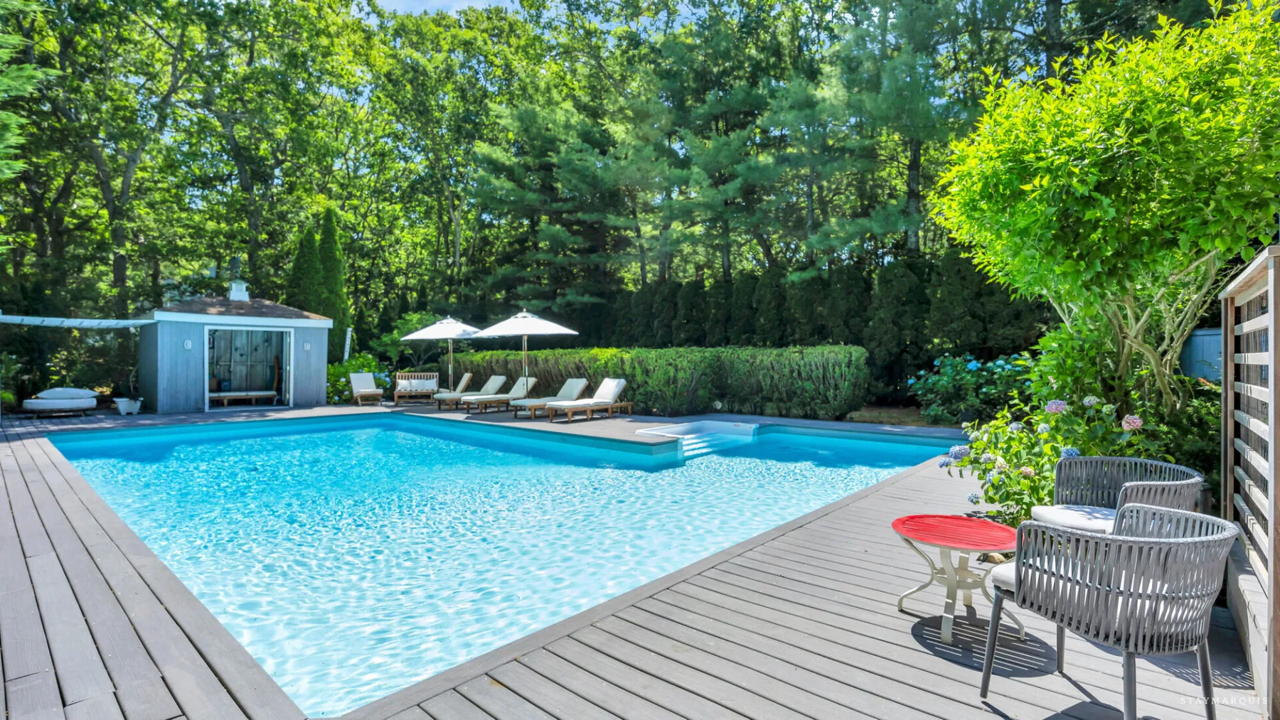 An outdoor swimming pool is surrounded by a wooden deck and greenery.