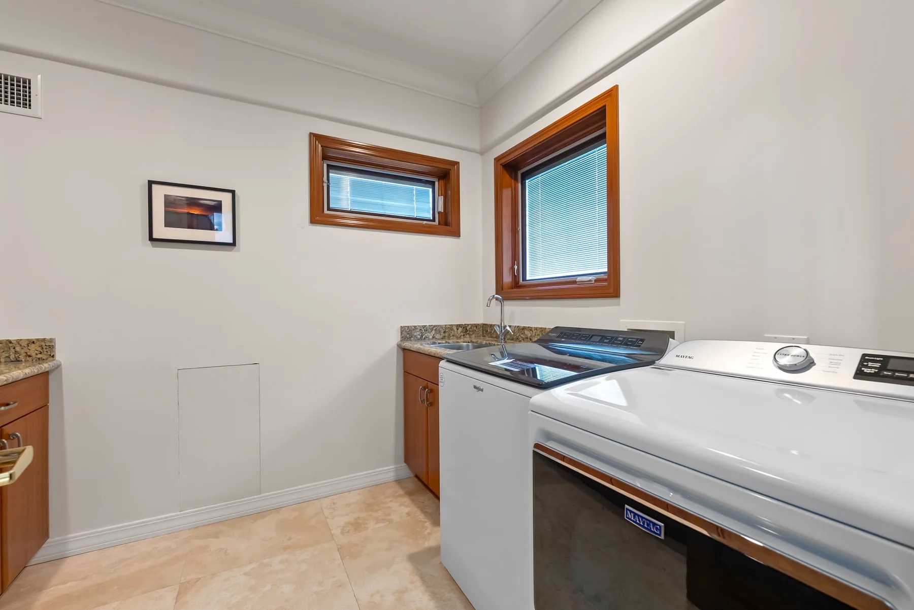 Un cuarto de lavandería con lavadora y secadora debajo de dos ventanas.