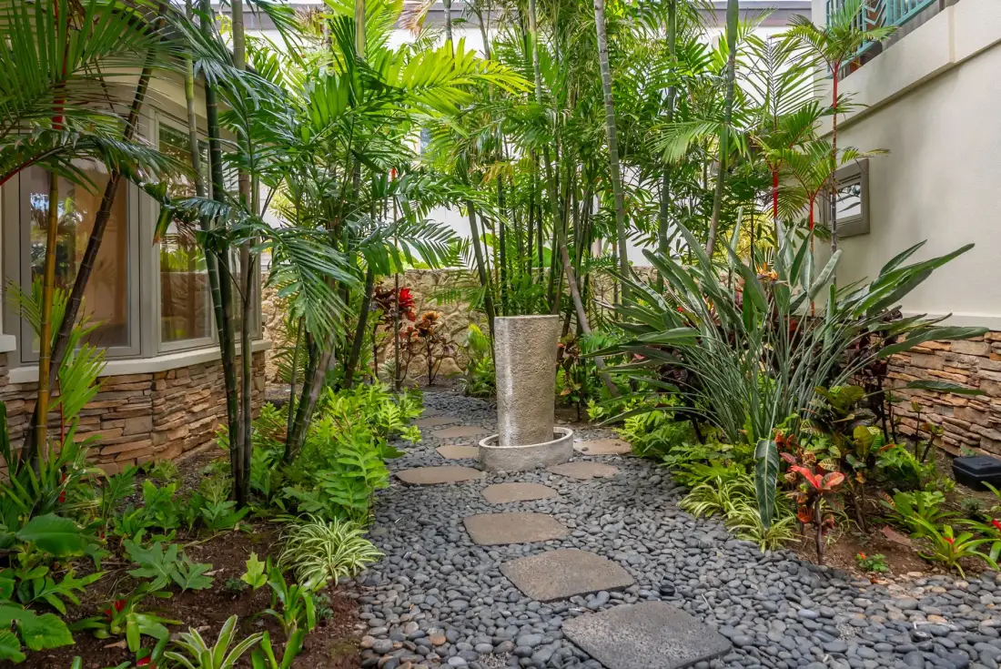Un patio ajardinado tiene un sendero de piedra entre plantas tropicales.