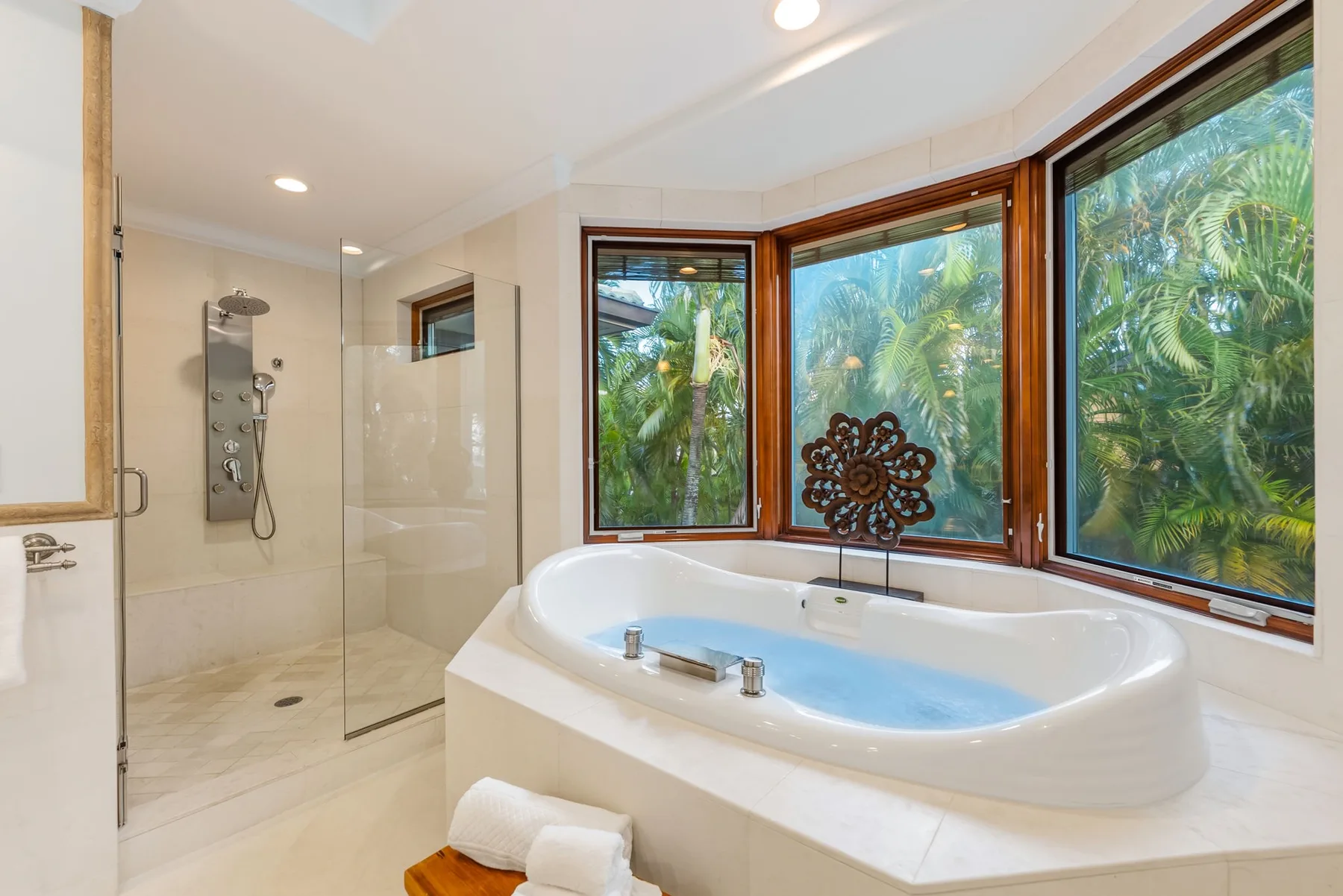 Un baño luminoso con bañera junto a una ducha con mampara de vidrio y ventanas grandes.