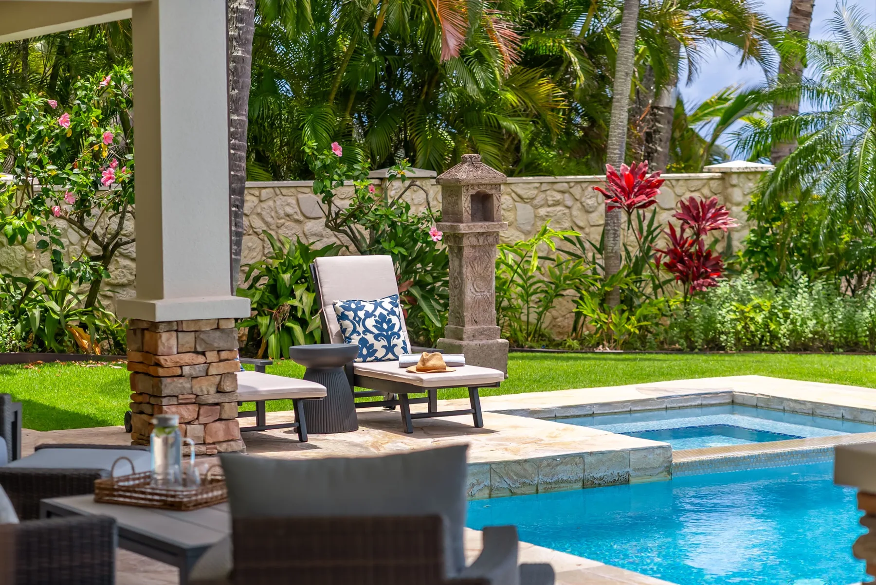 Un patio de jardín tropical da a una piscina, con asientos acolchados cerca.