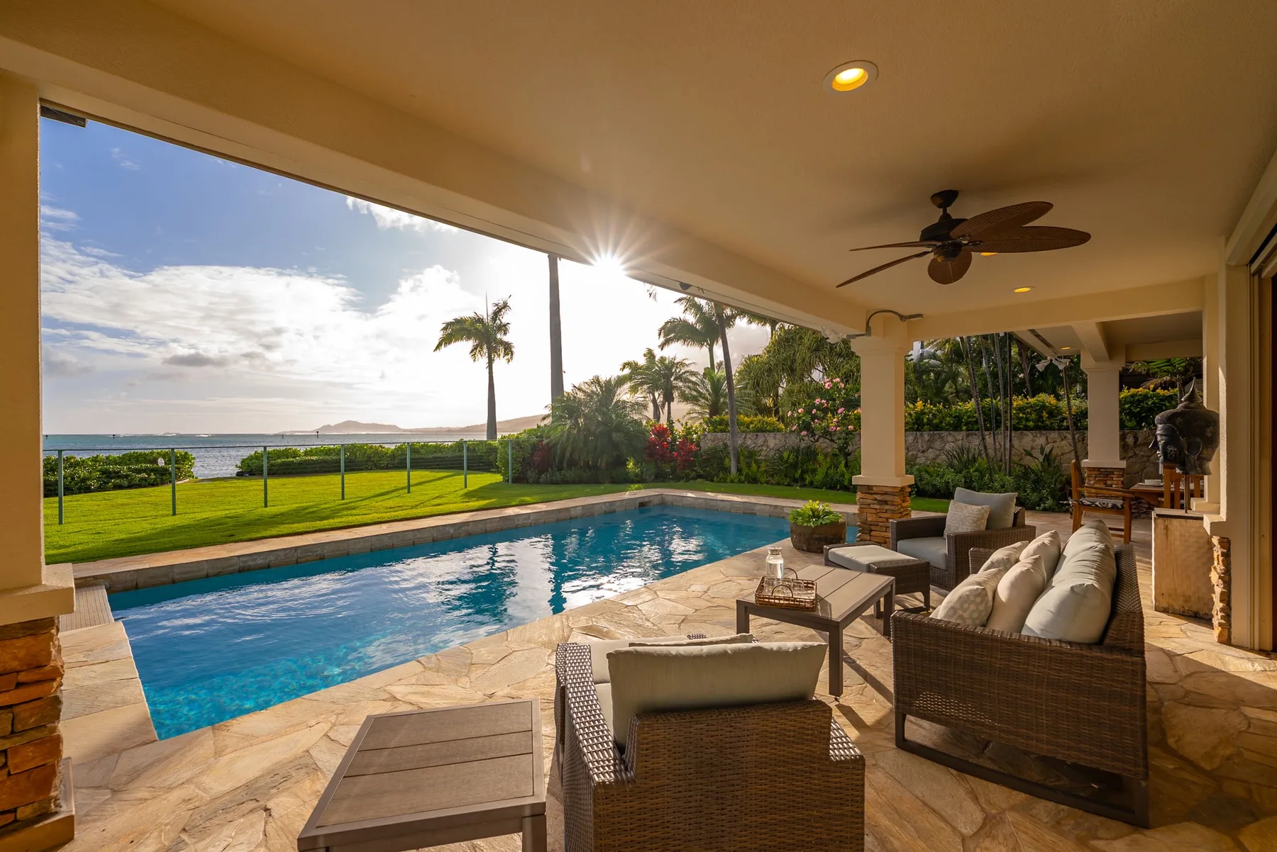 Un patio cubierto con asientos da a una piscina y jardines.