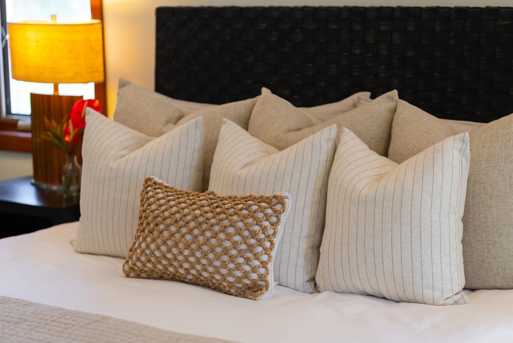 Una cama bien arreglada con almohadas superpuestas y un cabecero oscuro tapizado.