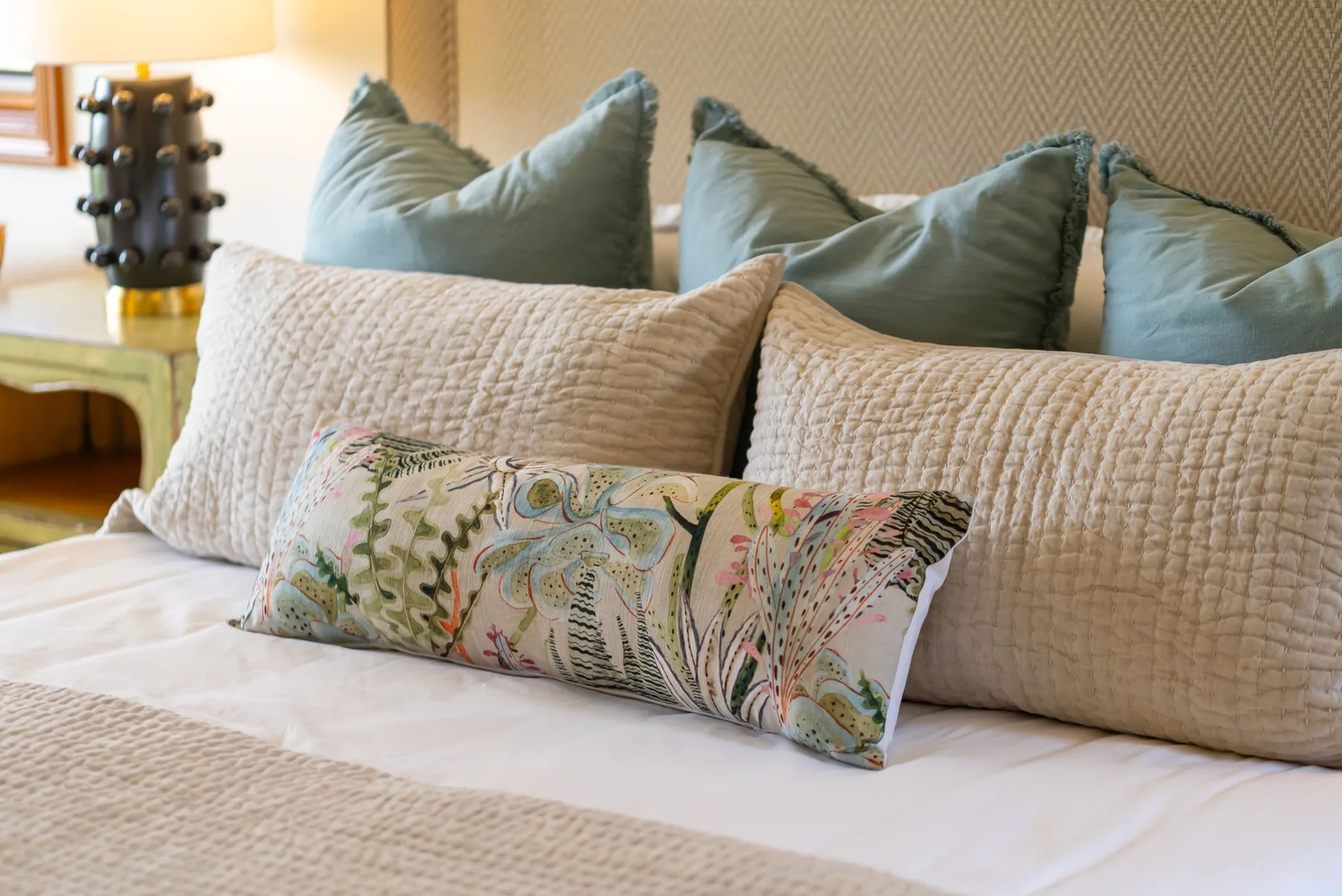 Una cama bien arreglada con almohadas superpuestas y un cojín decorativo estampado.