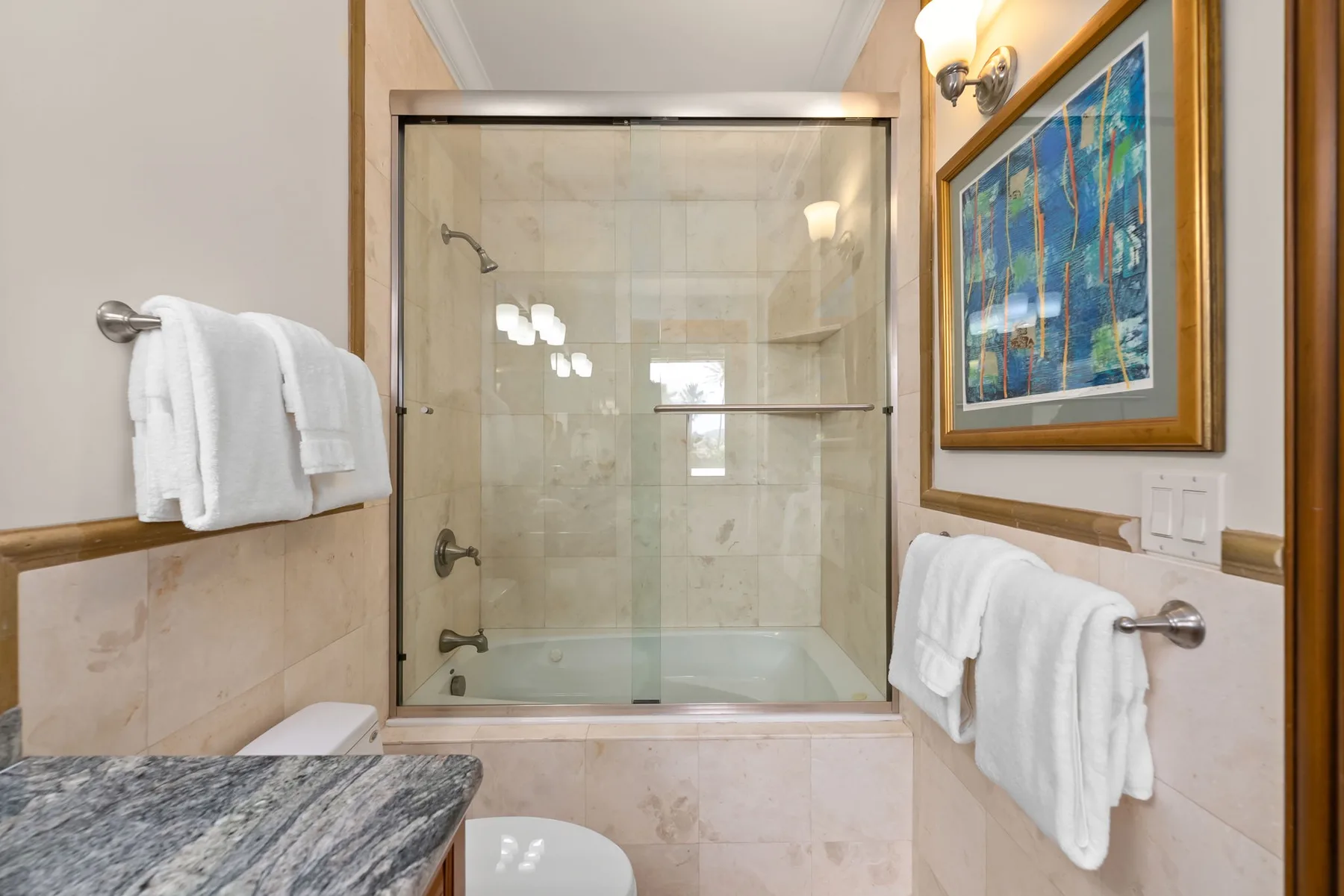 Un baño con una ducha de vidrio y toallas blancas colgadas en las paredes.