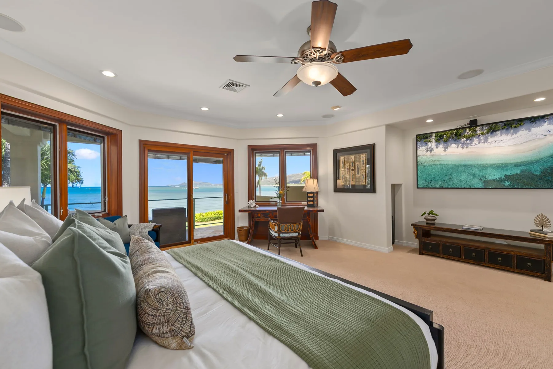 Un dormitorio con una cama, un ventilador de techo y vistas al mar por las ventanas.