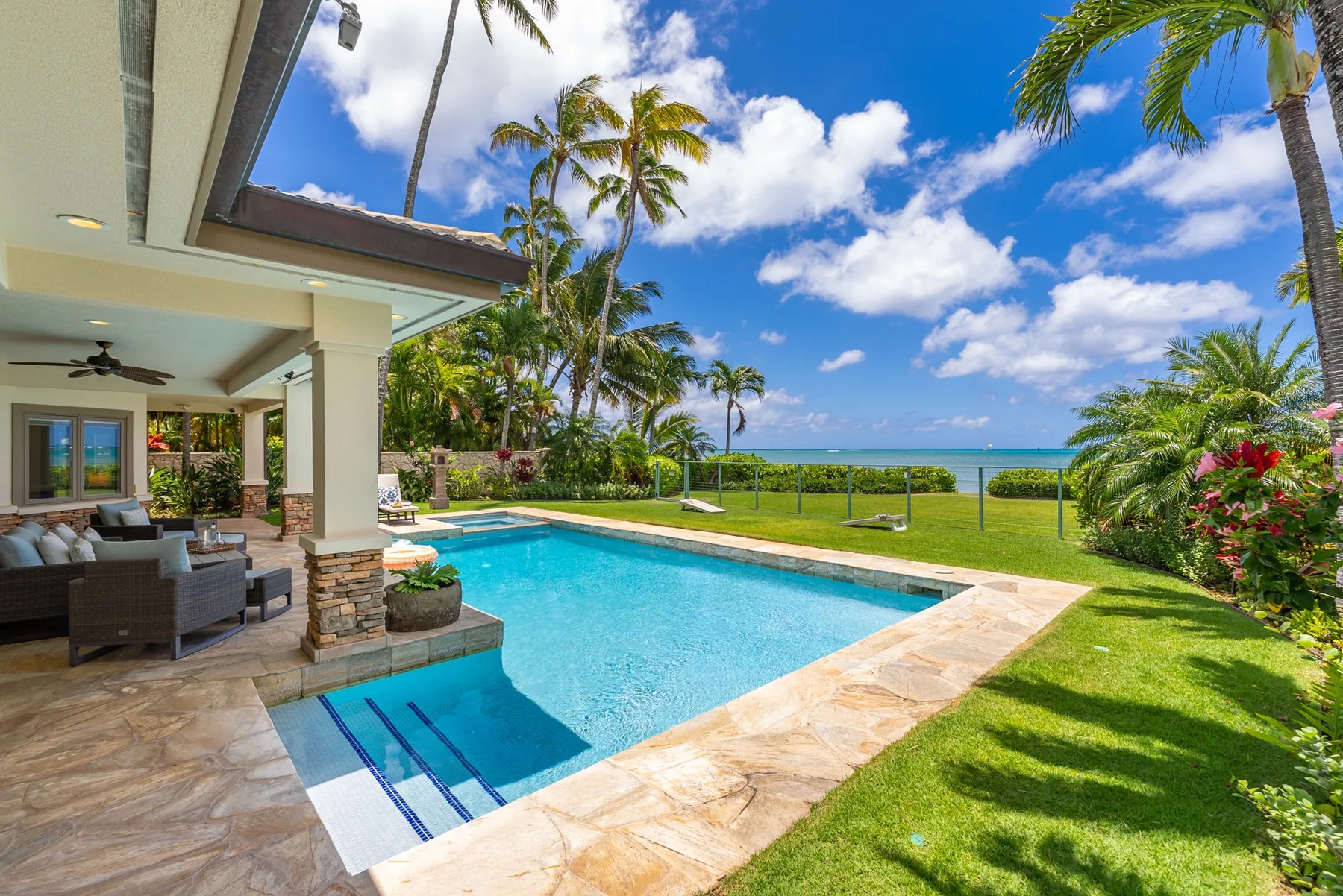 Una piscina al aire libre junto a un patio cubierto y vegetación tropical.