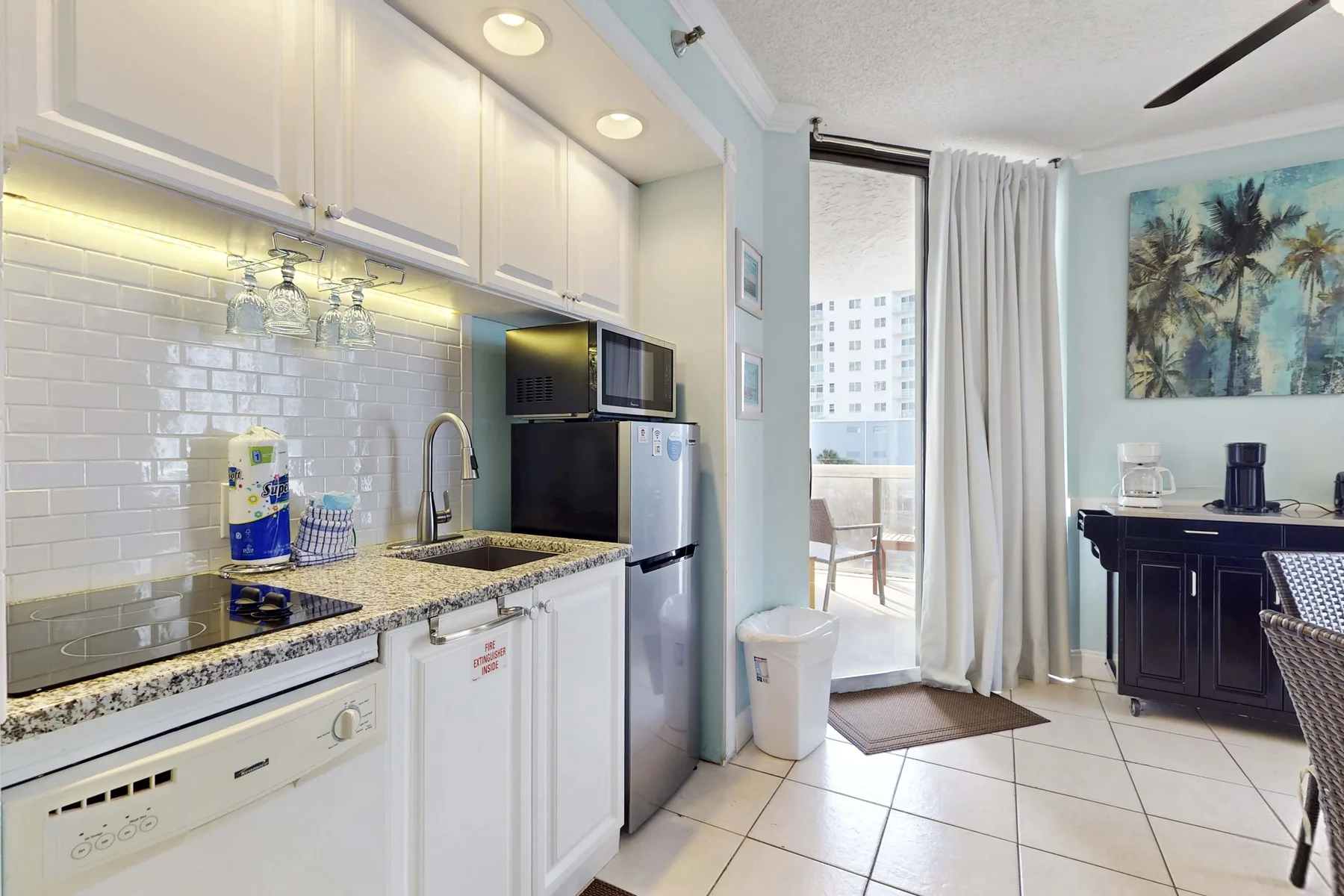 Una cocina luminosa con gabinetes blancos se abre a un balcón junto a un comedor.