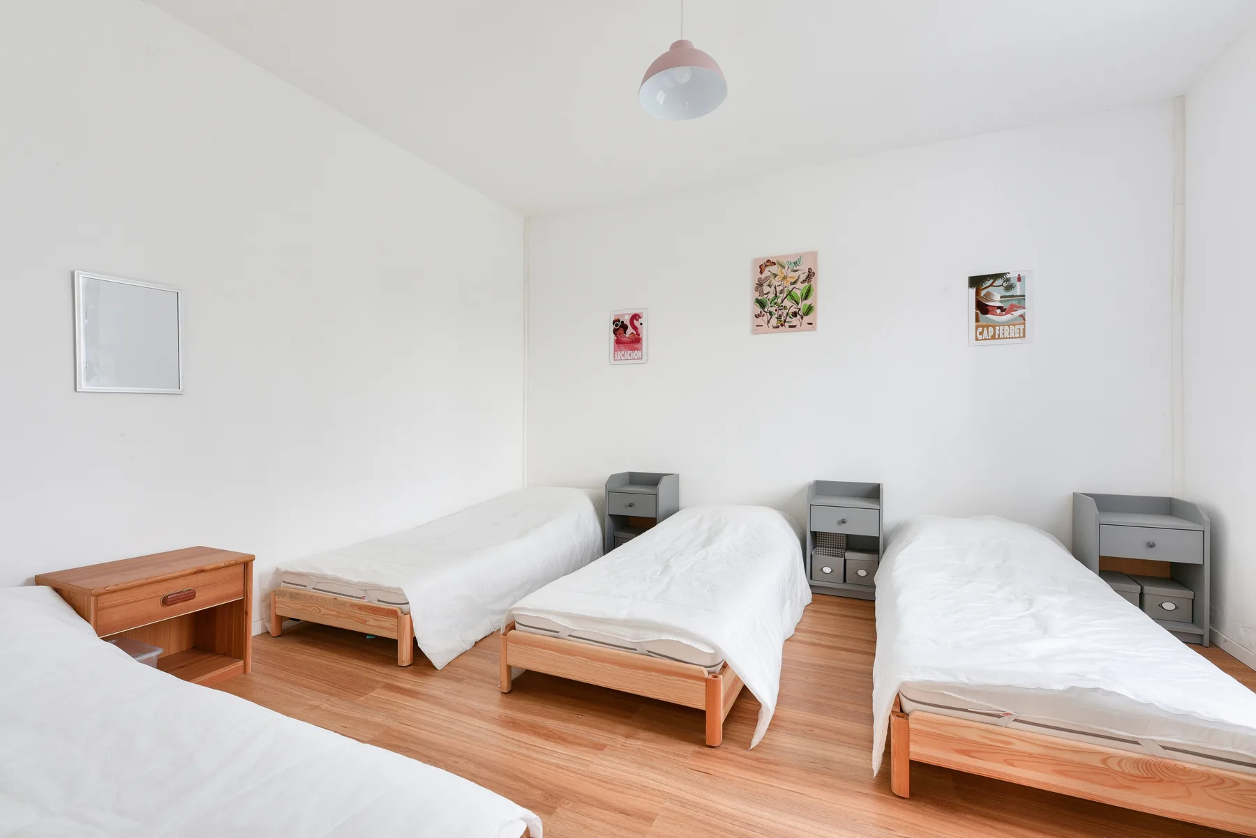 A bright bedroom with several single beds and simple wall art.