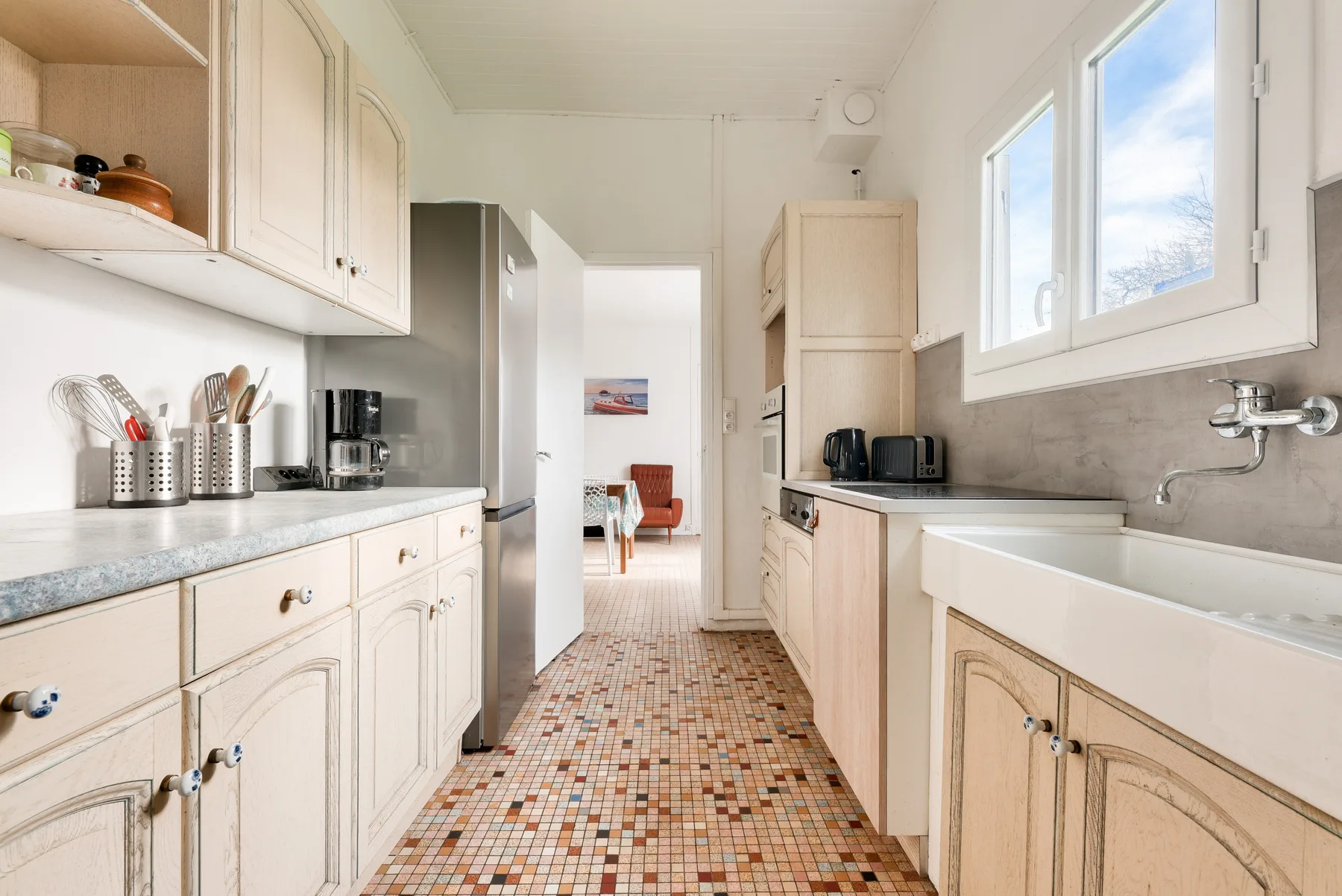 A bright kitchen with pale cabinets and a tiled floor.