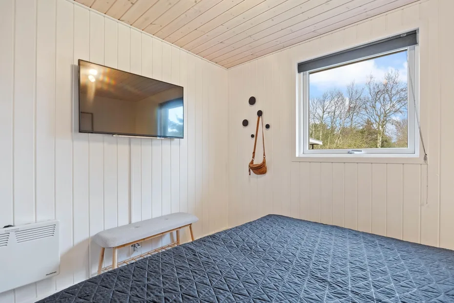 Un dormitorio con una cama, un televisor en la pared y una ventana con vista a los árboles.