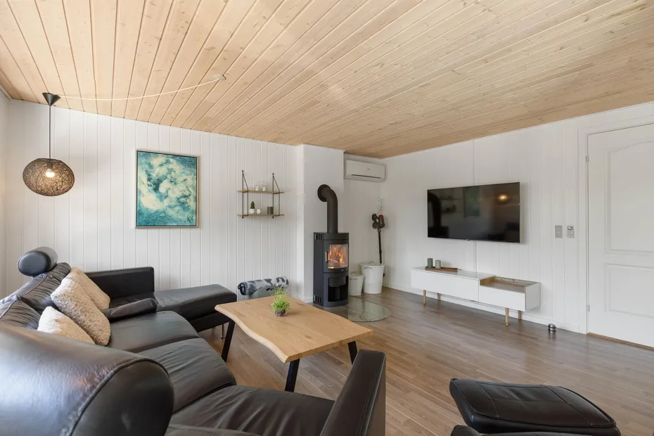 Una sala de estar con asientos oscuros, una mesa de centro de madera y un televisor en la pared.
