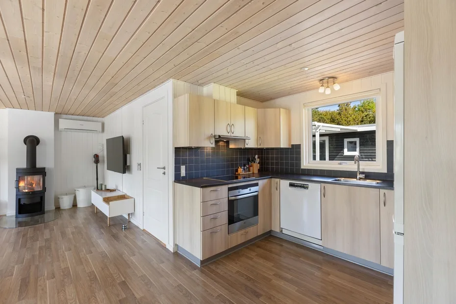Una cocina compacta y zona de estar con muebles de madera clara y una estufa negra.