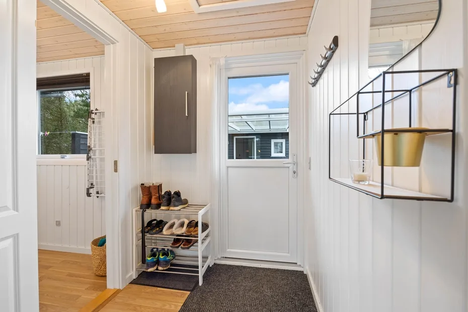 Una entrada luminosa con un zapatero junto a la puerta exterior.