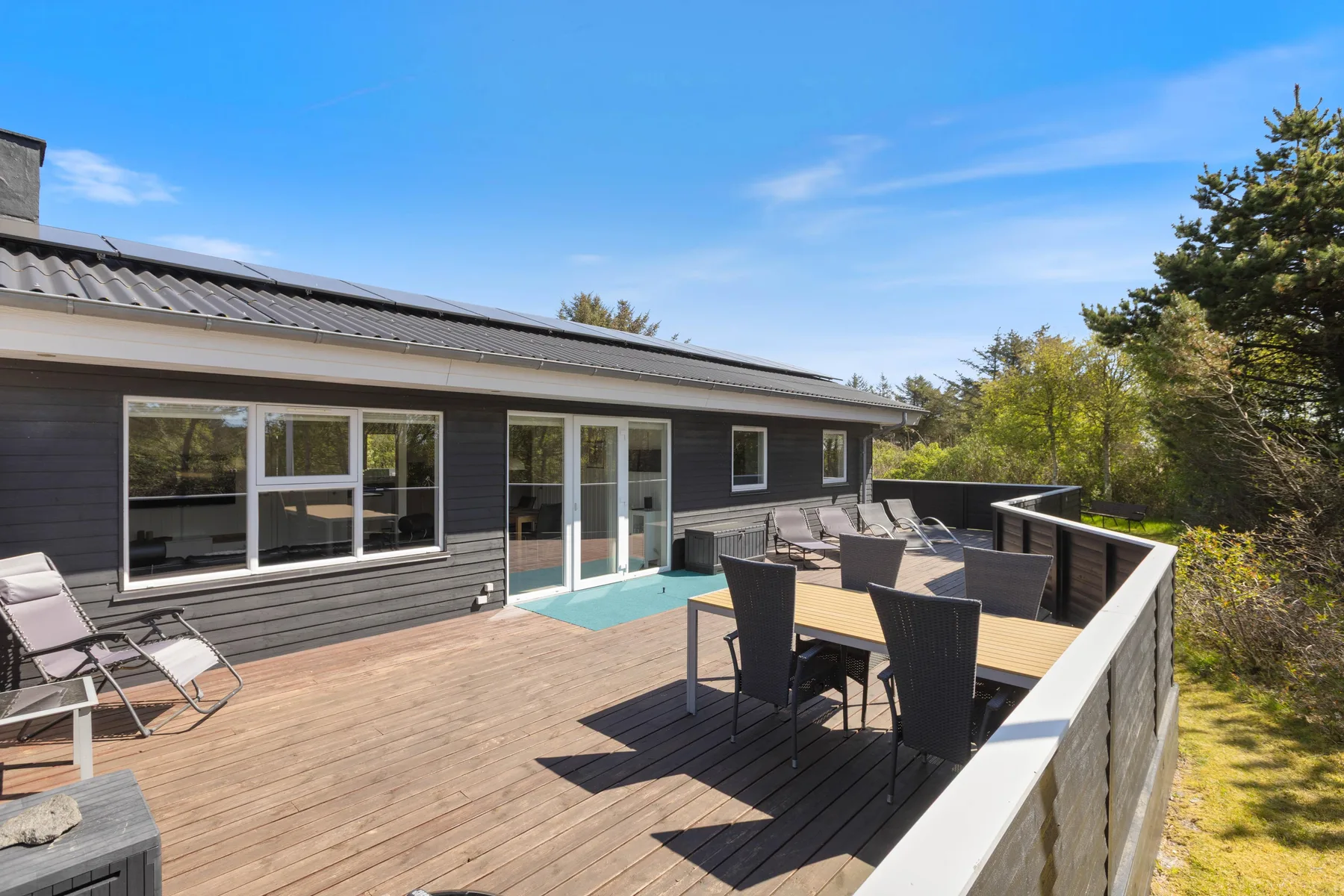 Una terraza de madera con asientos al aire libre y una mesa de comedor junto a la casa.