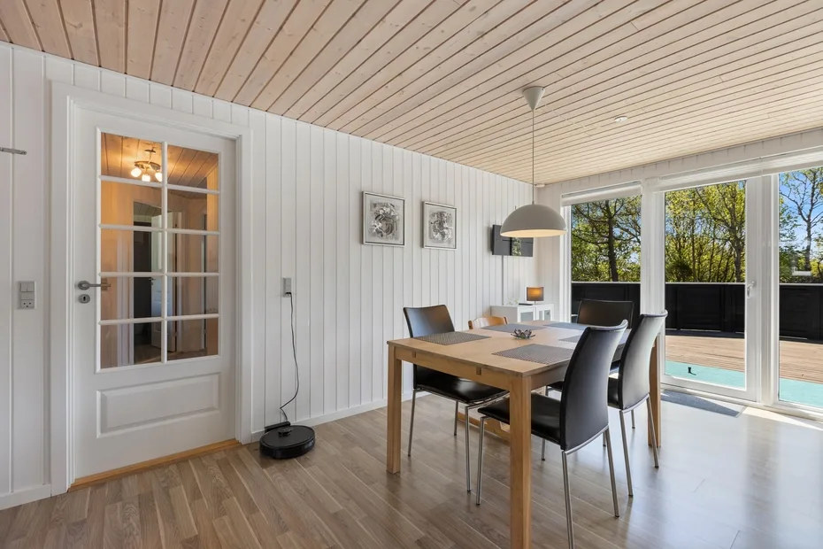 Comedor con una mesa de madera y grandes ventanales con vistas a una piscina.