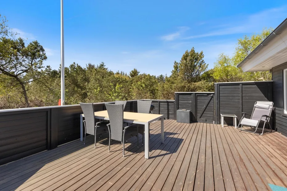 Una terraza exterior con mesa y asientos da a árboles frondosos.
