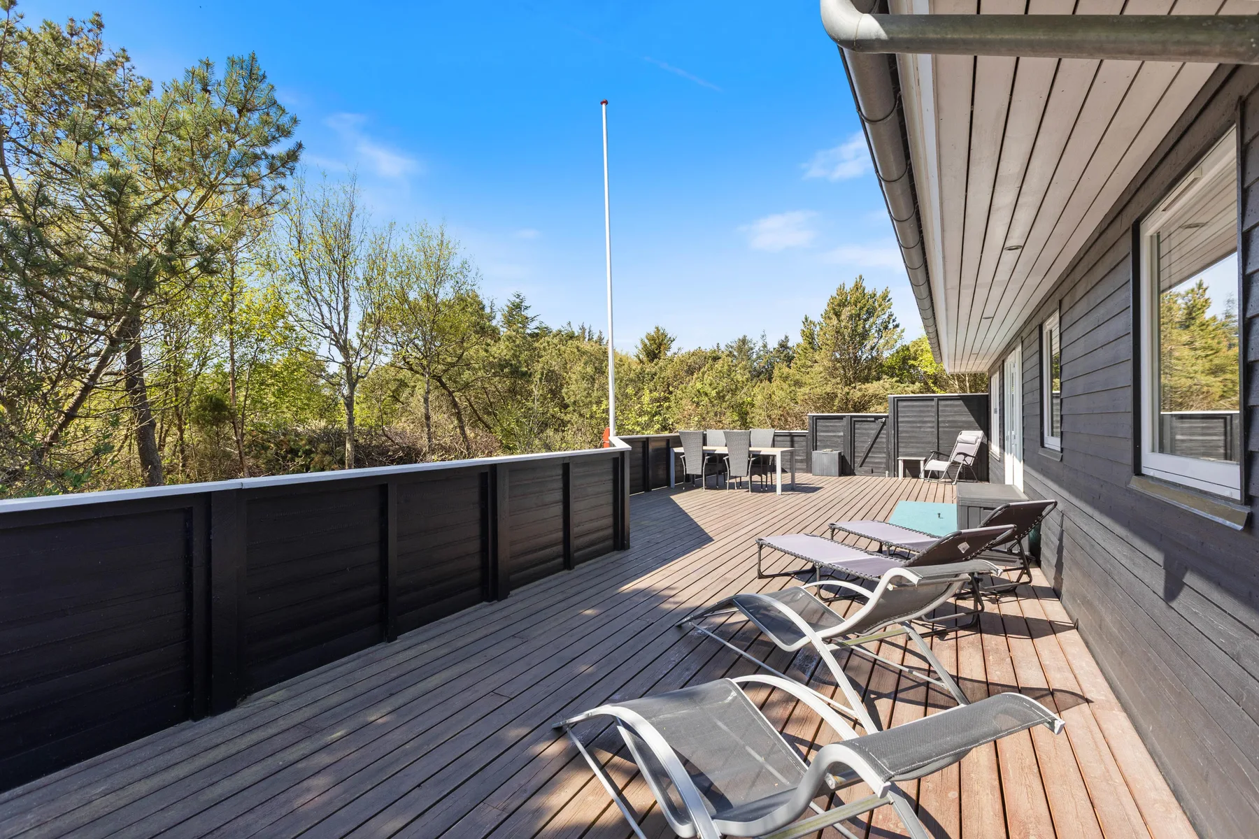Una terraza de madera junto a una casa tiene asientos al aire libre y da a unos árboles.