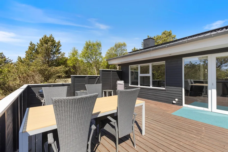 Una terraza en la azotea con mesa de comedor y asientos al aire libre junto a una casa moderna.