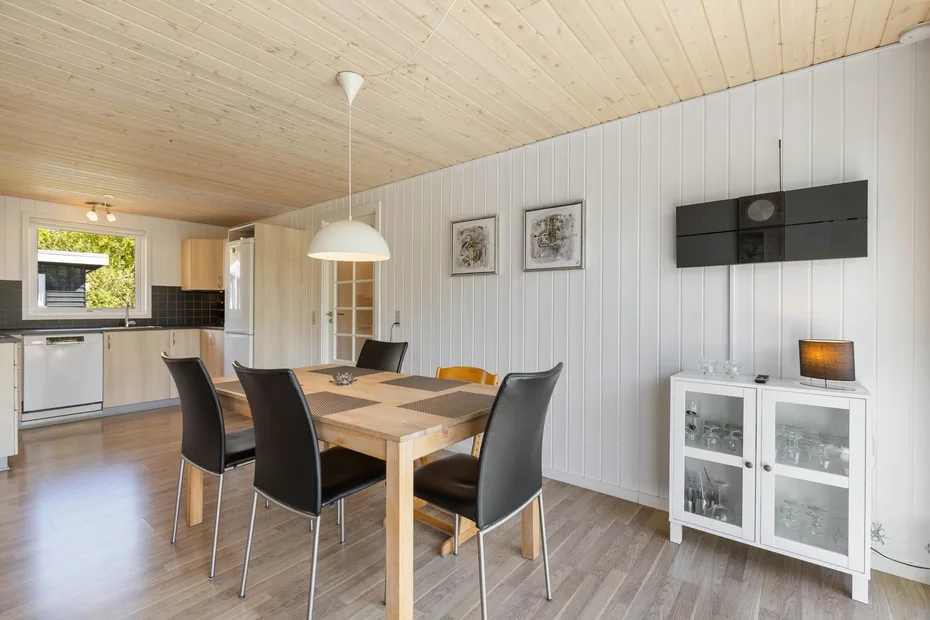 Comedor con una mesa de madera y sillas negras junto a una cocina abierta.