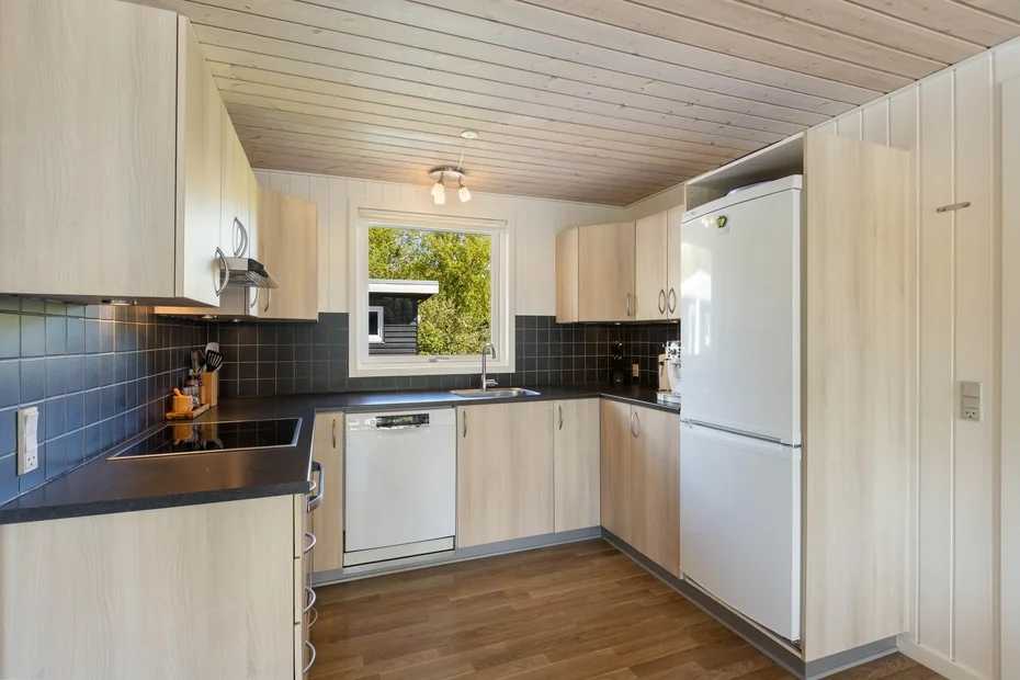 Una cocina luminosa con gabinetes de madera clara, encimeras oscuras y una ventana.