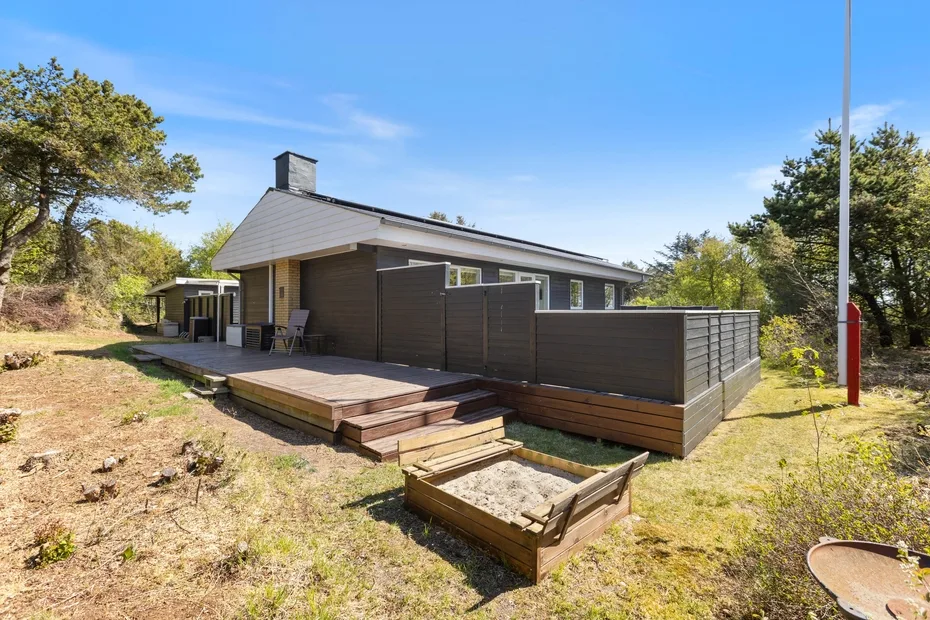 Una casa moderna de una planta tiene una terraza elevada de madera y un patio cercado.