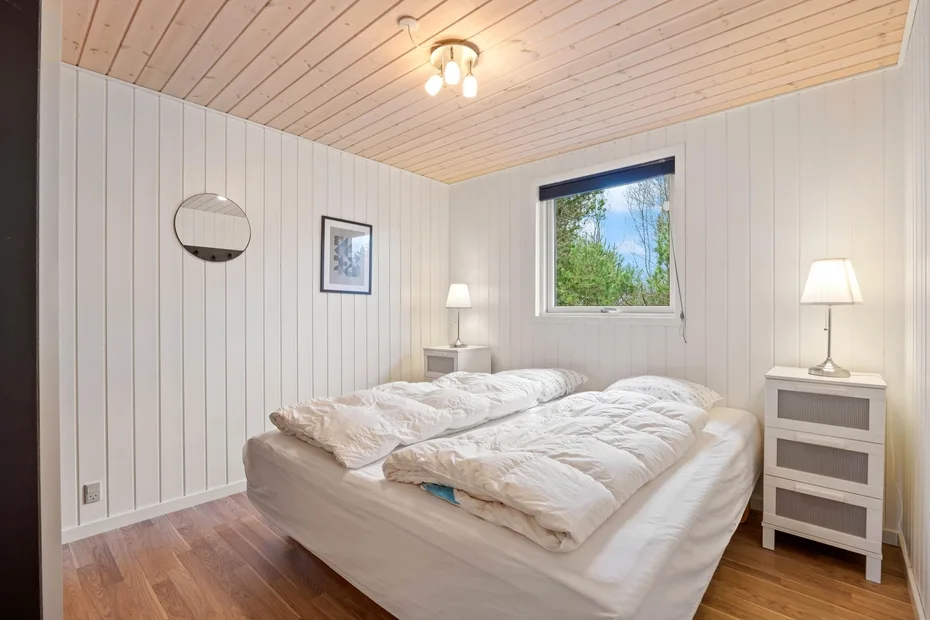 Un dormitorio con una cama bajo una ventana con vistas a la vegetación.