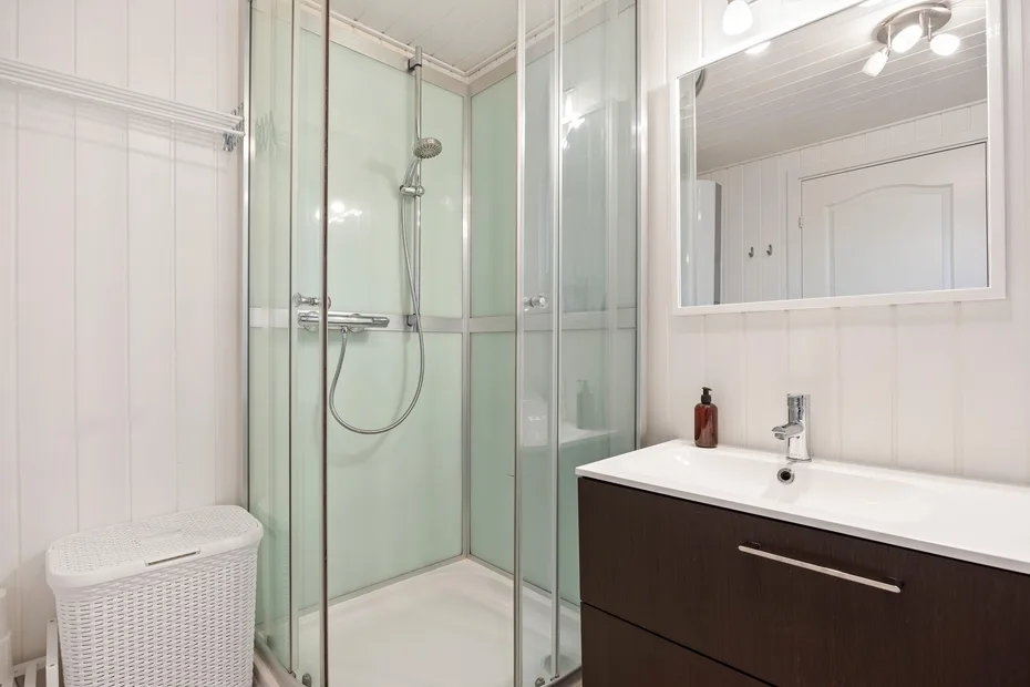 Un baño luminoso con ducha de vidrio y un tocador bajo un espejo grande.