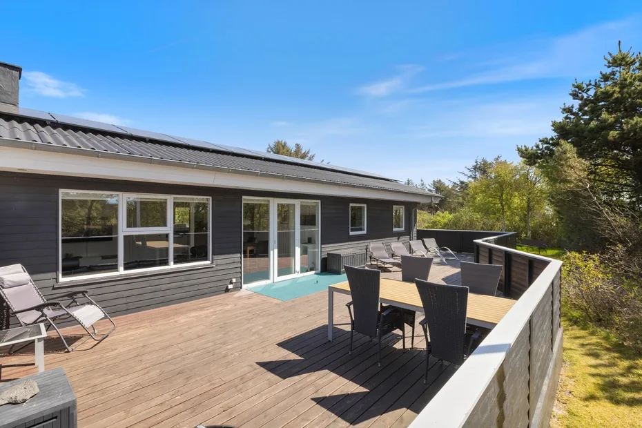 Una terraza de madera junto a una casa moderna tiene una mesa de comedor y asientos.