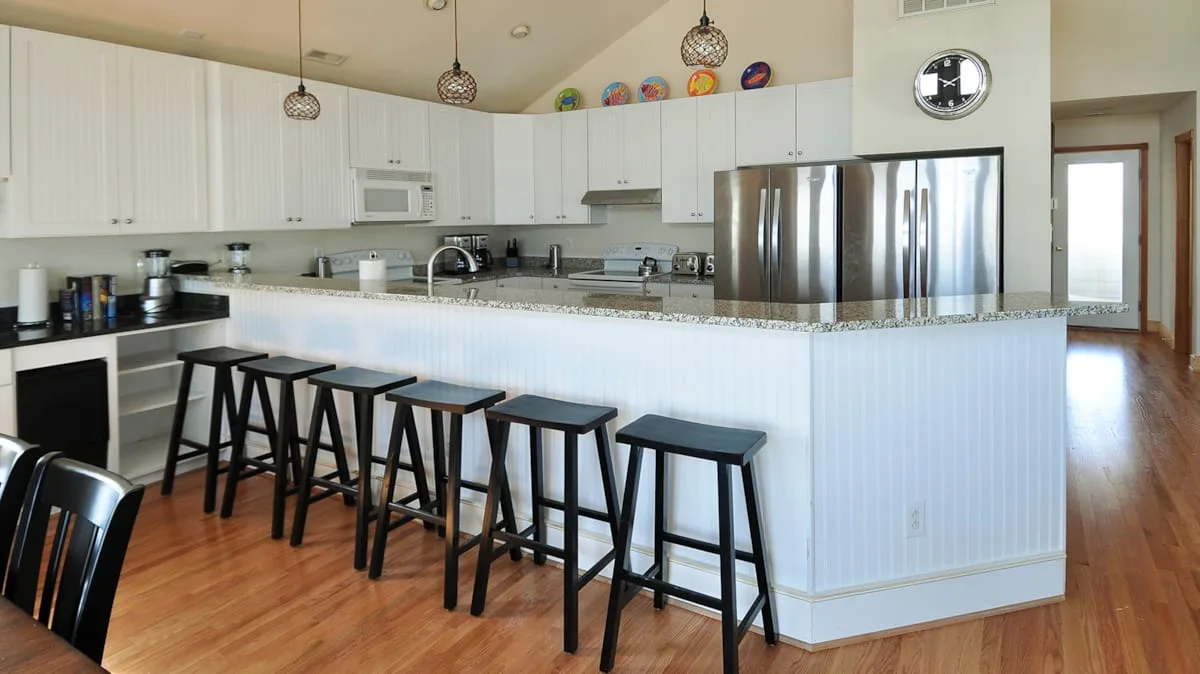 A bright kitchen with white cabinets, stainless steel appliances, and a long counter.