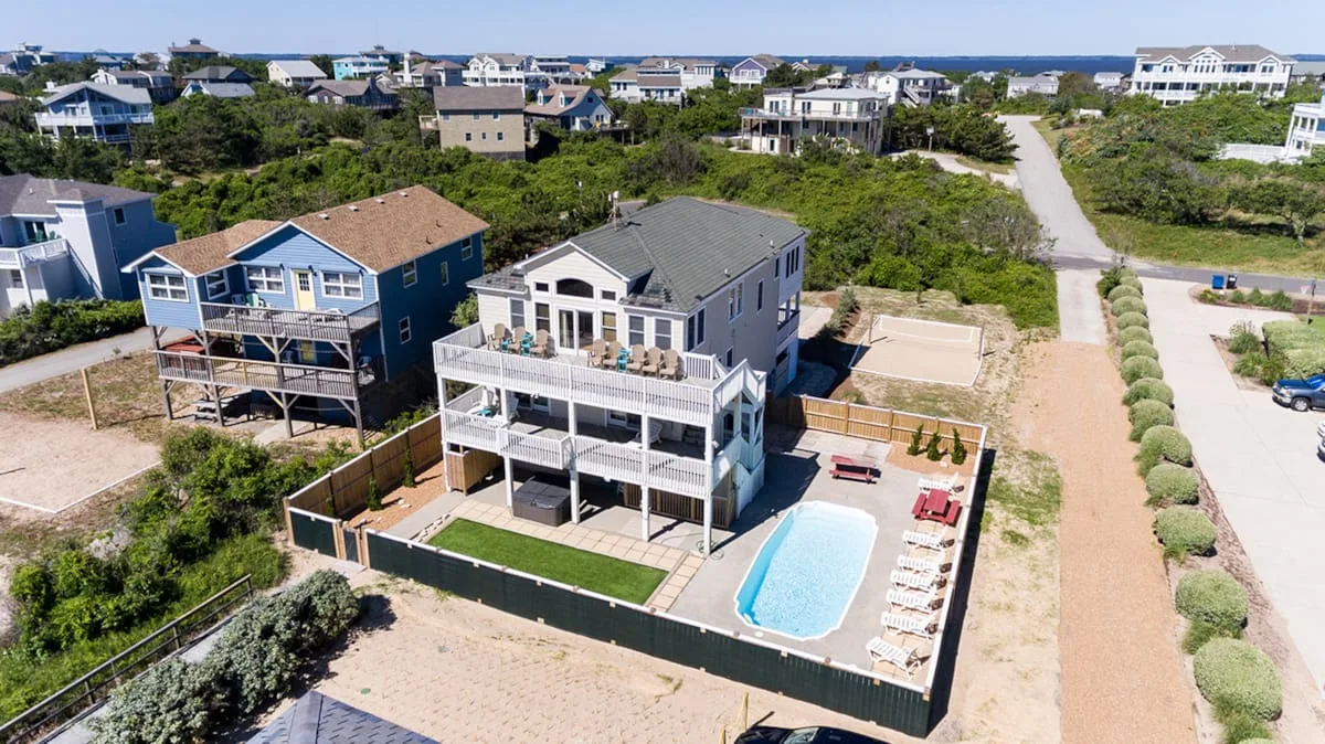 Aerial view of a coastal neighborhood with a large house, pool, and surrounding greenery.