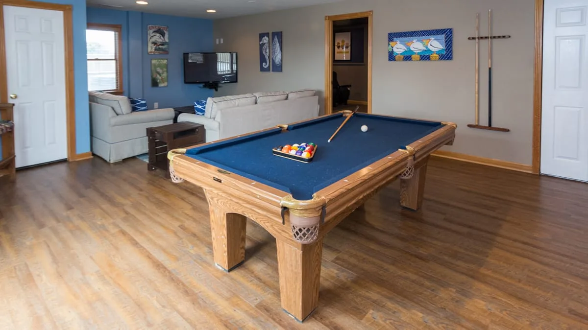 Una sala de juegos cuenta con una mesa de billar, con asientos y un televisor al fondo.