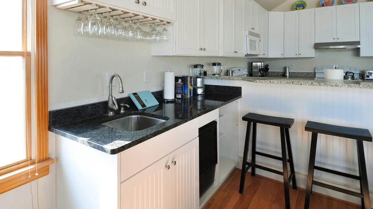 A bright kitchen with a black countertop, sink, and bar seating.