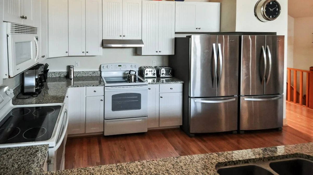 Una cocina con gabinetes blancos, electrodomésticos de acero inoxidable y piso de madera.