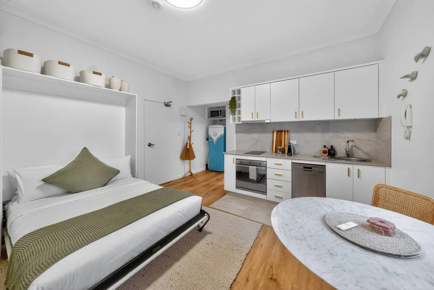 Un estudio luminoso con cama, cocina pequeña y mesa redonda.
