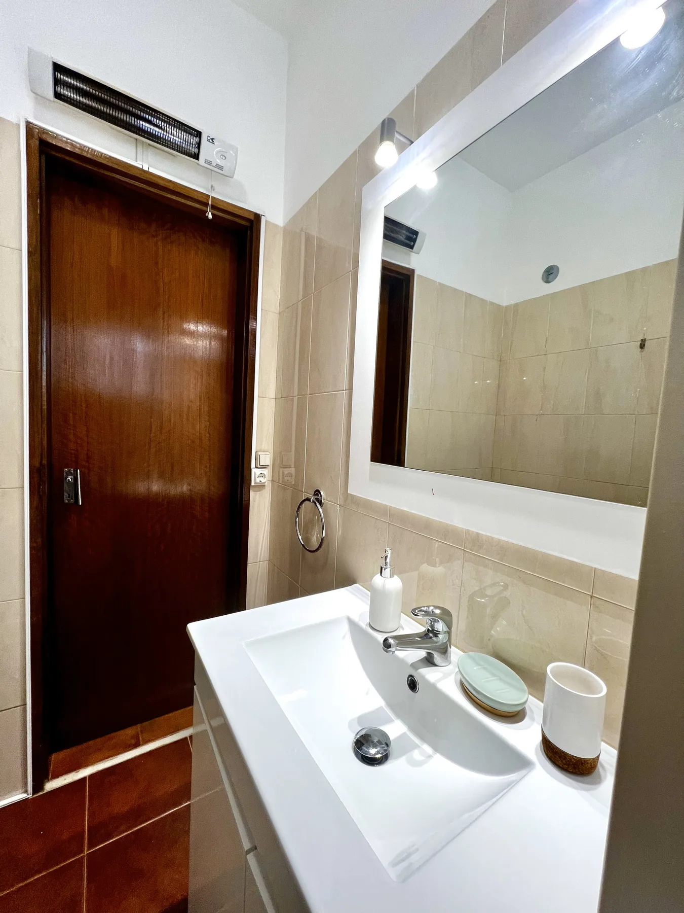 Un lavabo de baño con espejo junto a una puerta de madera.