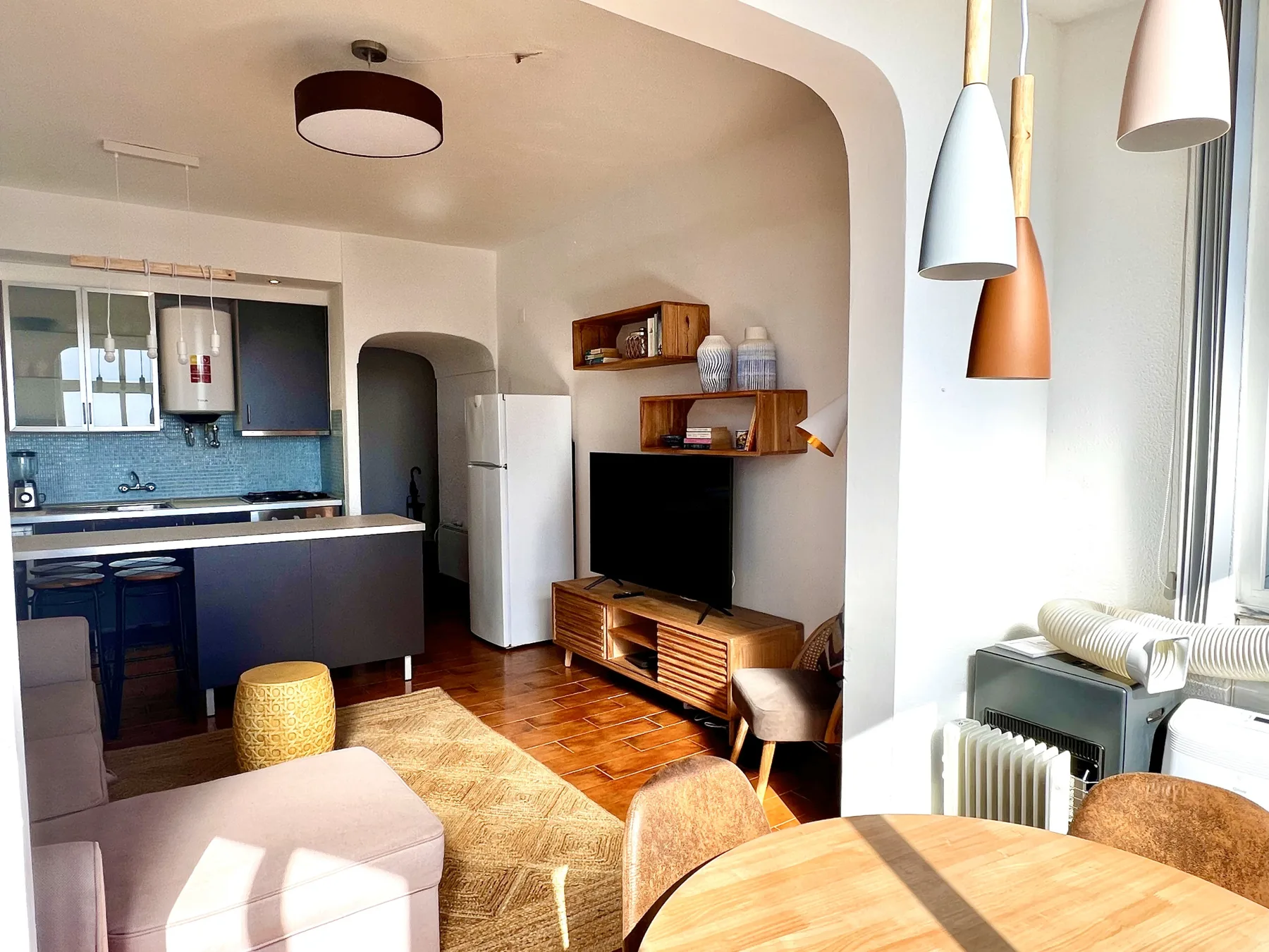 Una sala con comedor se abre a una cocina compacta, con un televisor y ventanales.