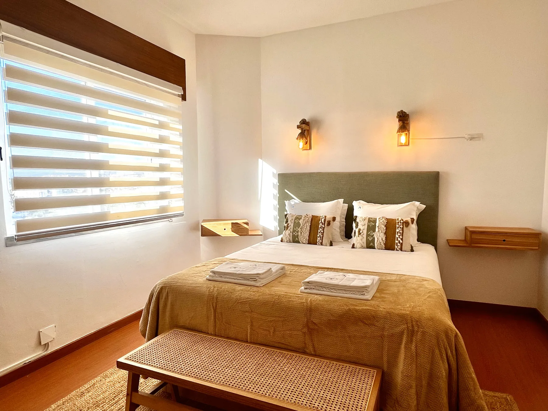 Un dormitorio con una cama bien tendida bajo dos luces de pared.