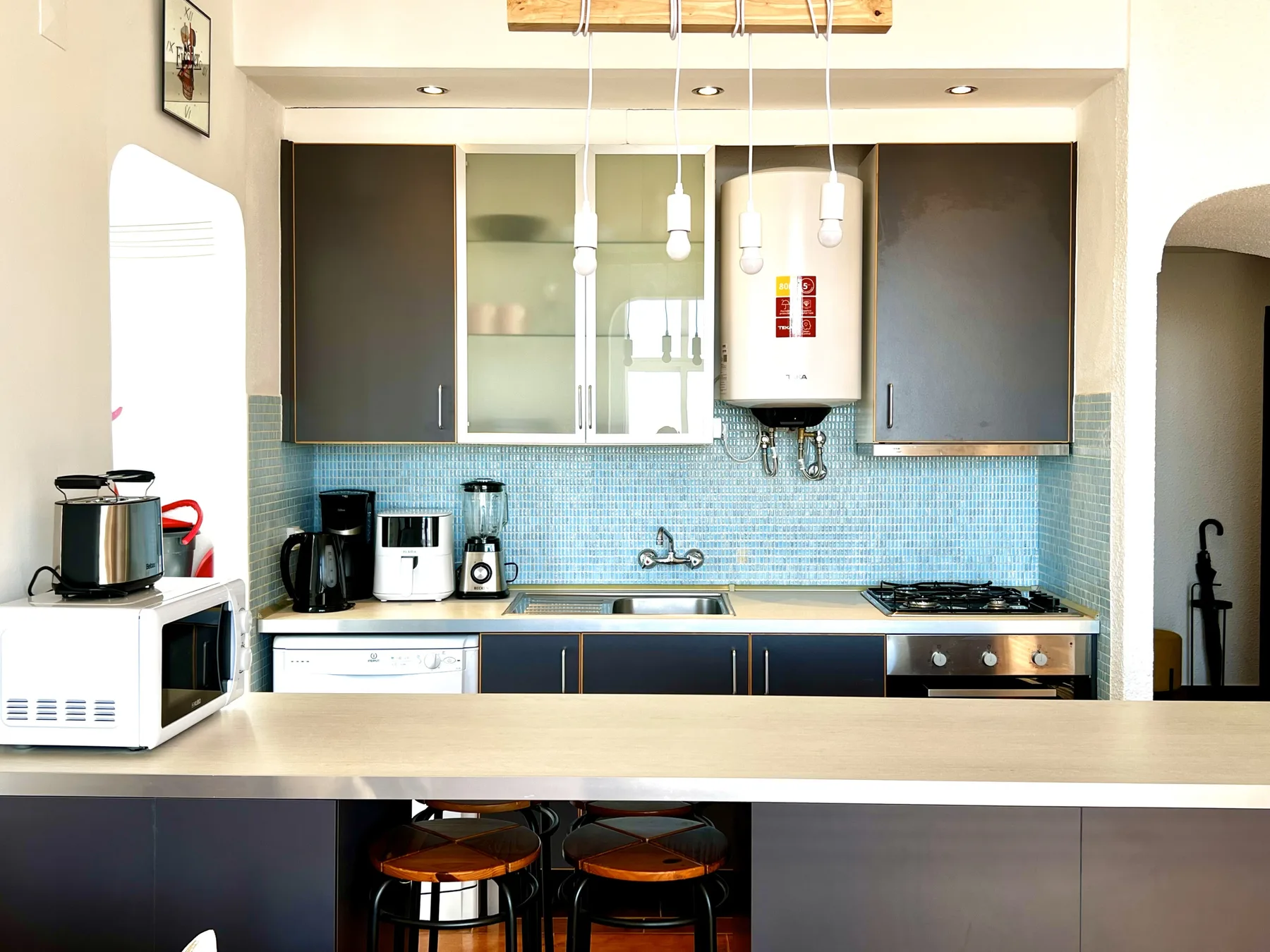 Una cocina luminosa con una barra larga, armarios oscuros y azulejos azules.