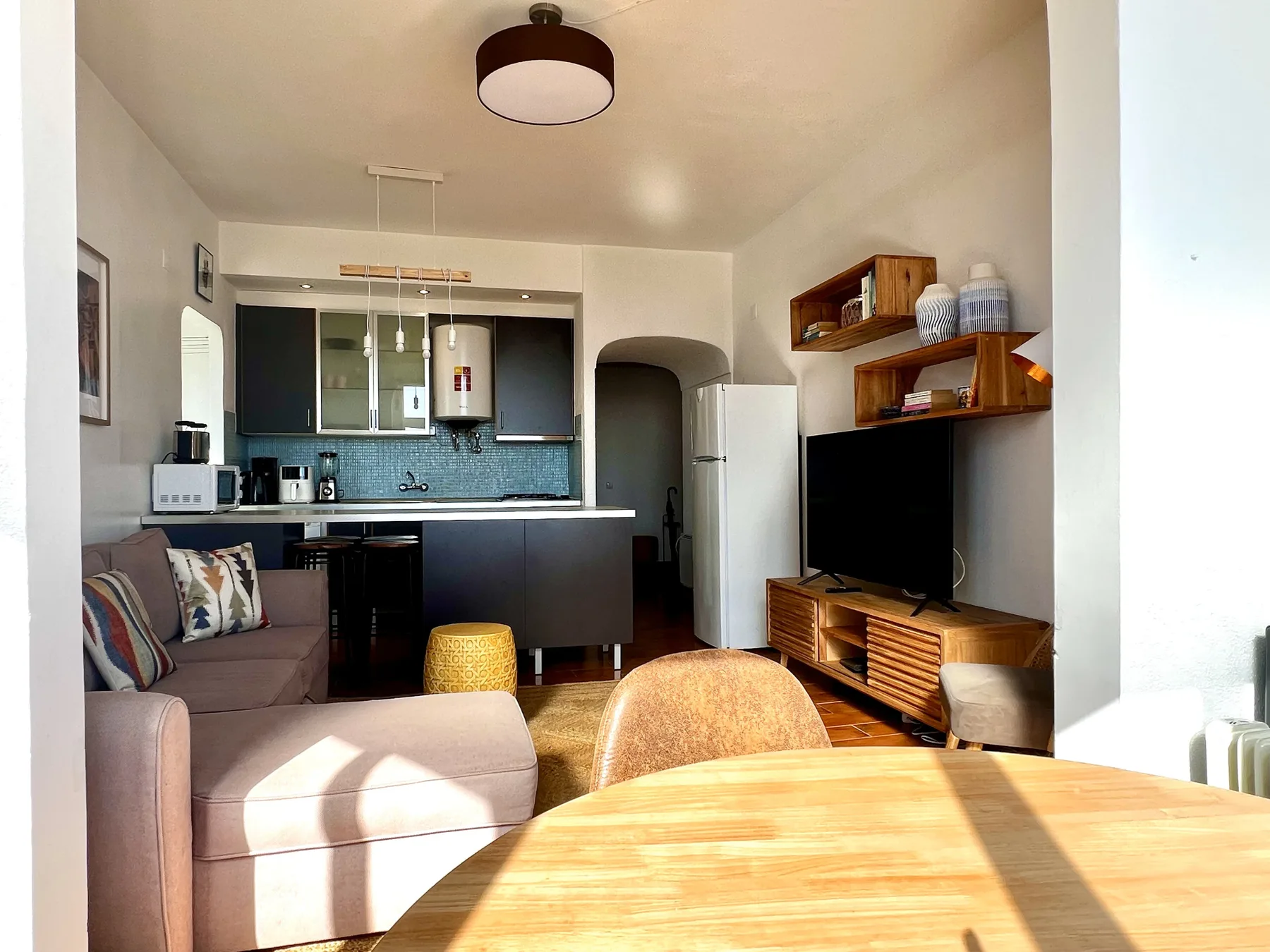 Una sala luminosa con zona de estar, televisor y cocina abierta.