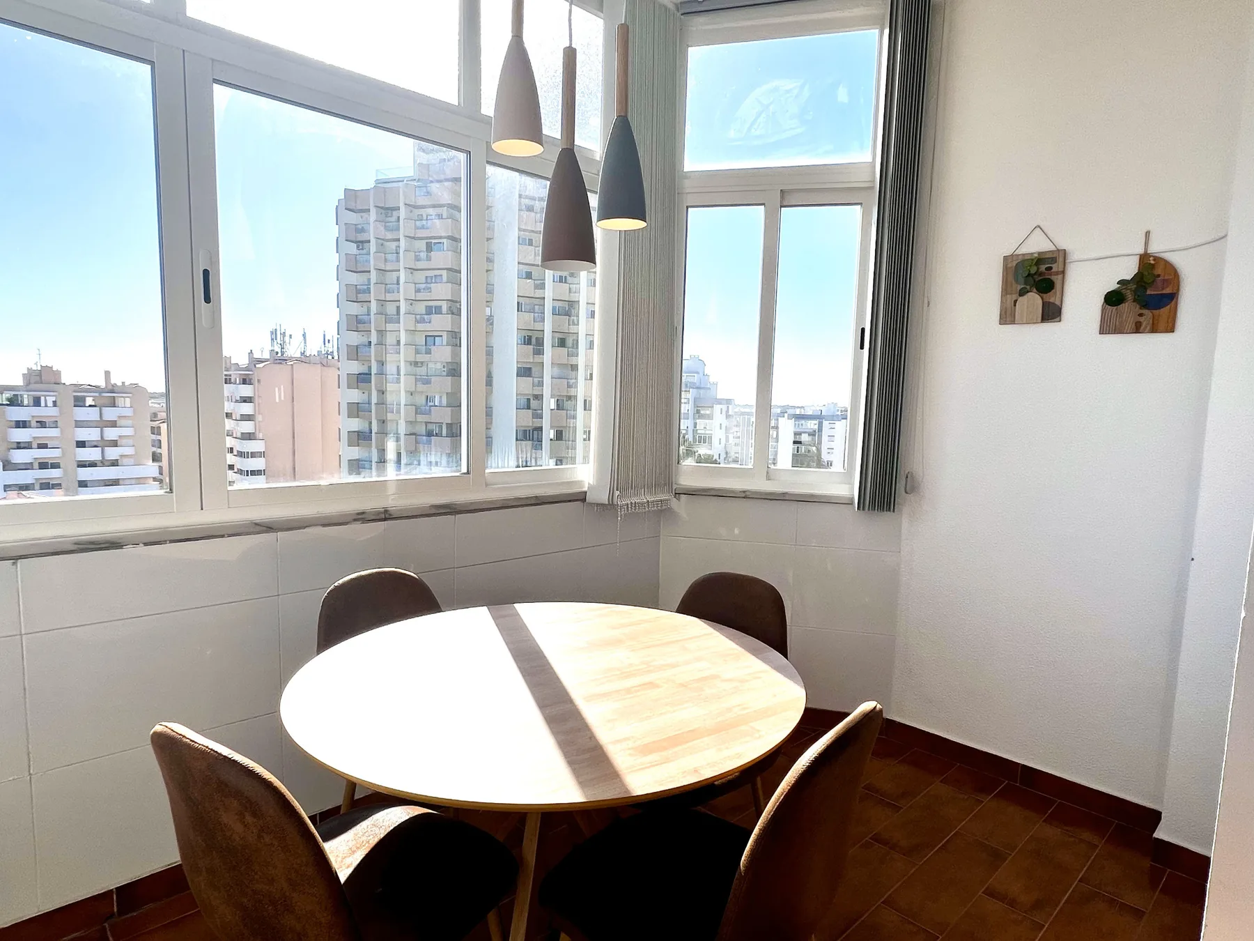 Comedor con una mesa redonda y grandes ventanas con vistas a edificios cercanos.