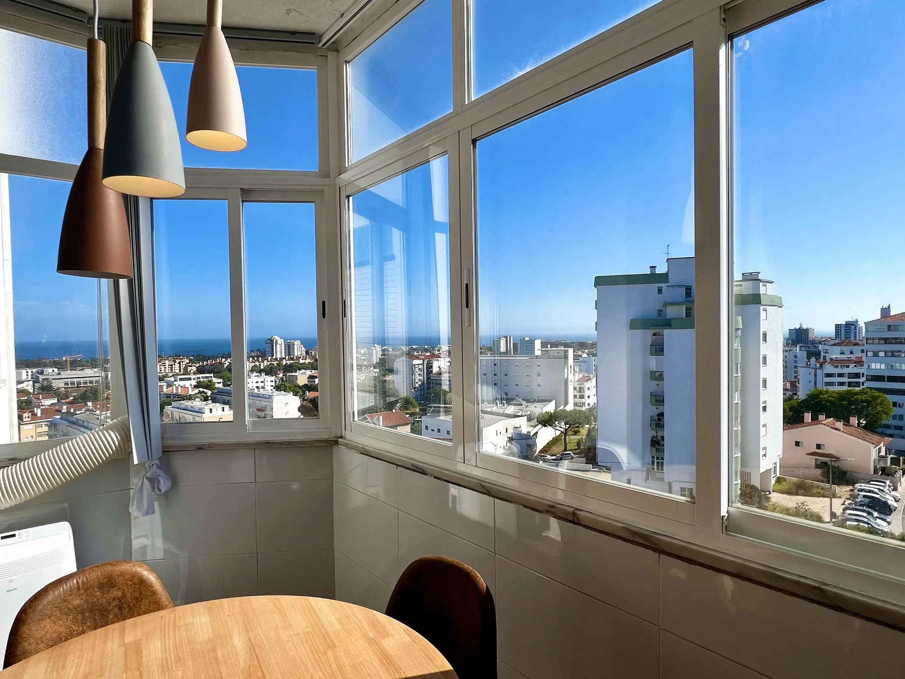Un comedor luminoso con grandes ventanas que dan a edificios cercanos y a la costa.