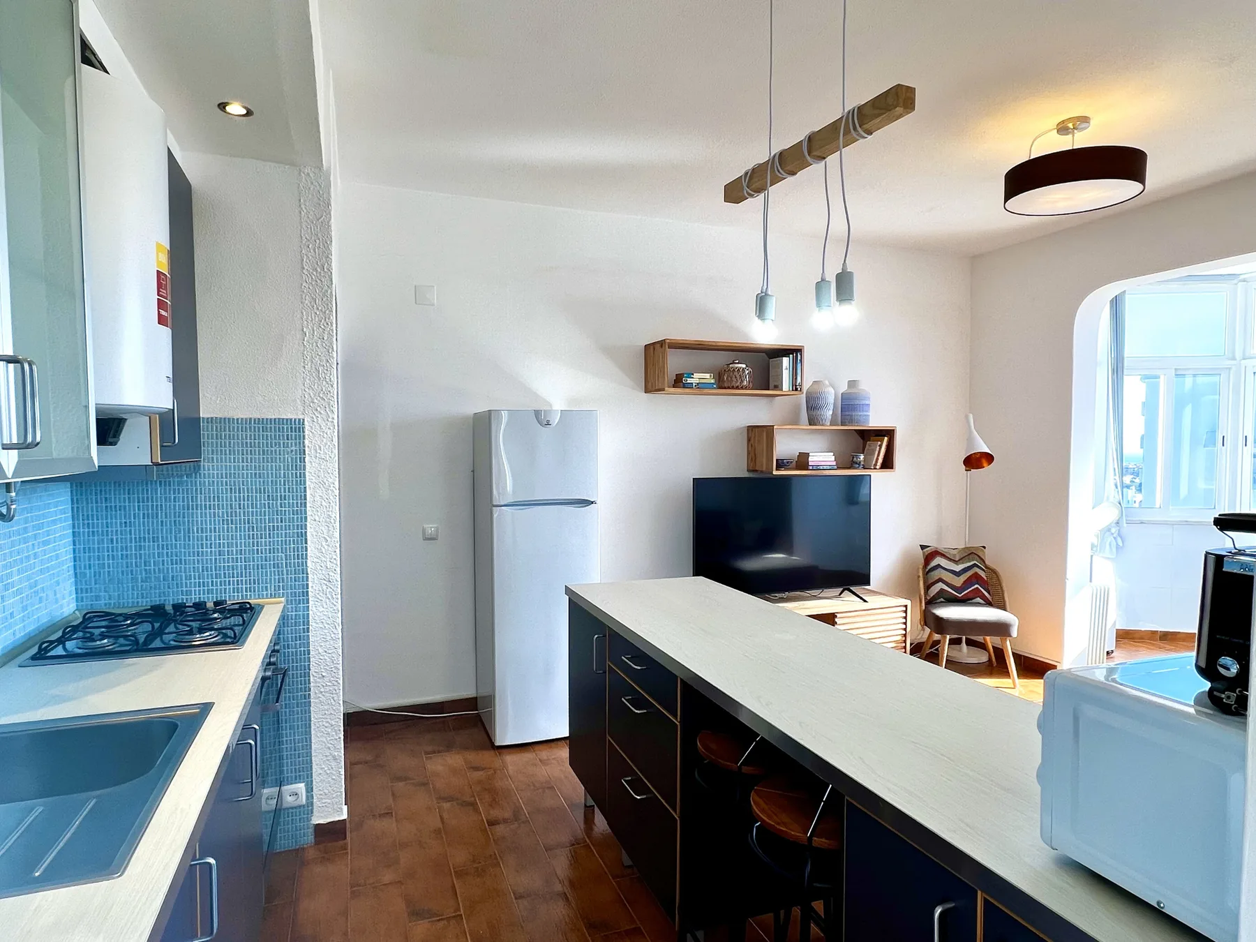 Cocina y comedor con una isla alargada, un refrigerador y un televisor.