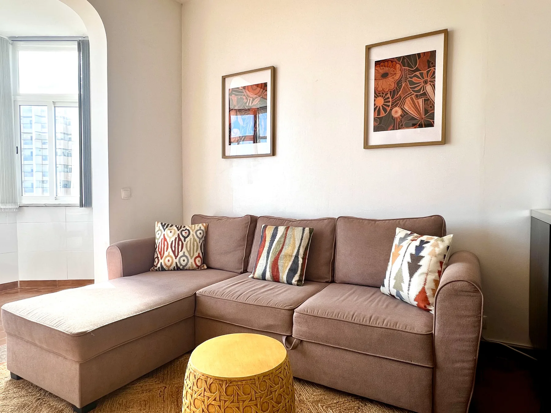 Una sala de estar con un sofá seccional, cojines coloridos y cuadros enmarcados.